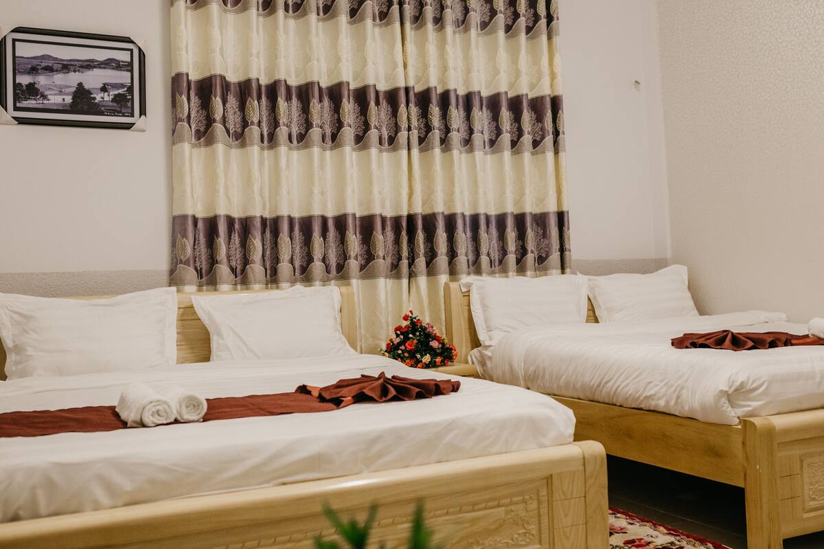 A hotel room with two beds, a framed picture on the wall, and a bouquet of flowers on the nightstand.