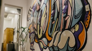 A room with a large abstract mural on the wall, a wooden cabinet, a potted plant, and a black speaker. - Levit'ss (Xuan Huong - Da Lat)