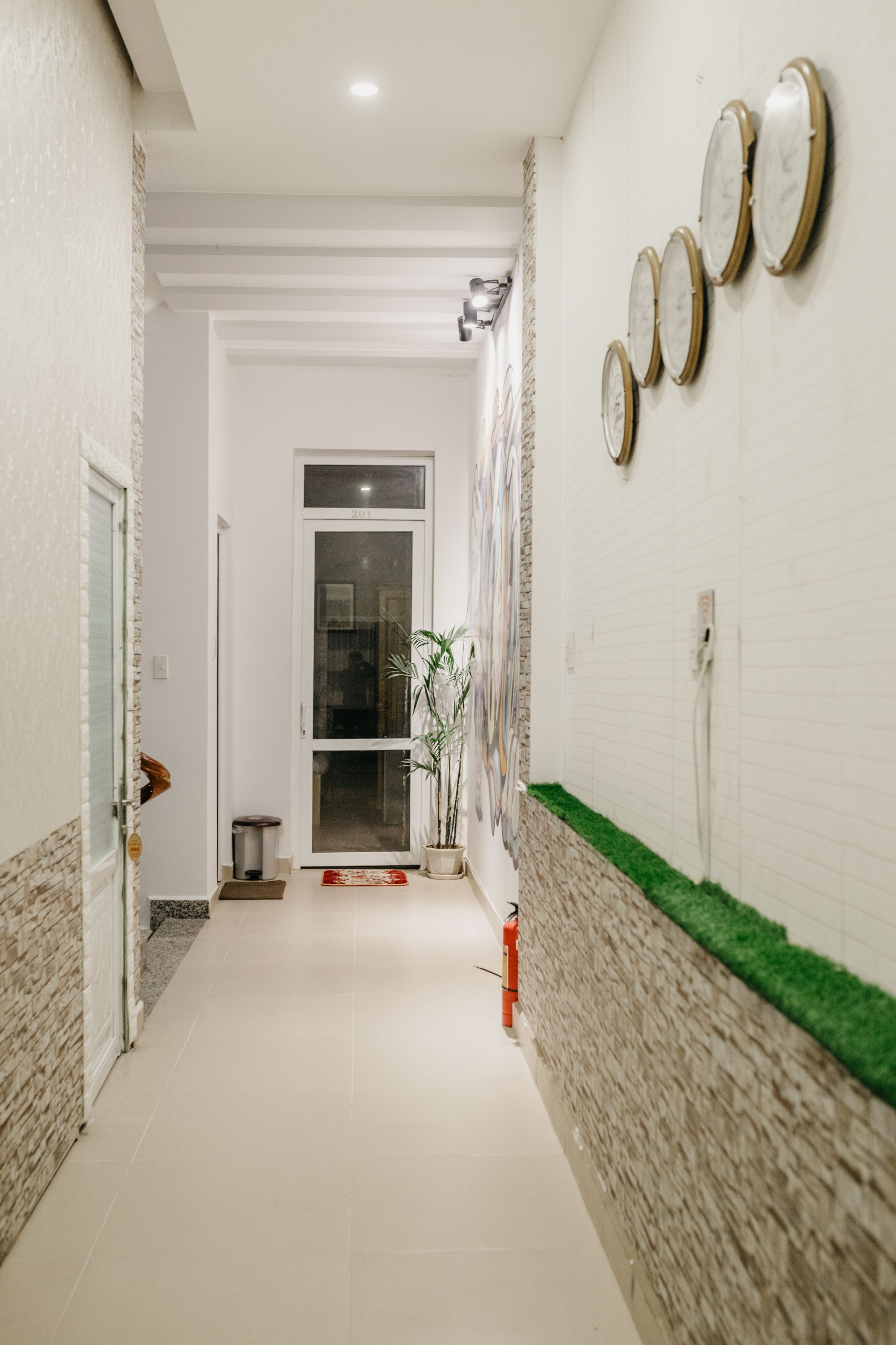 A hallway with a tiled floor, a fire extinguisher, a potted plant, and a door leading to a room.