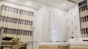 A bedroom with a bed, curtains, a floor lamp, and a small table. - Levit'ss (Xuan Huong - Da Lat)