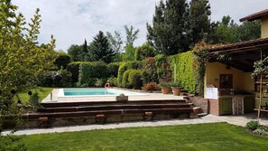 Une piscine accessible par des marches, entourée d’un jardin bien entretenu où l’on trouve diverses plantes et arbres.