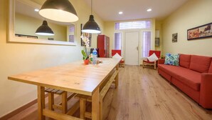 A dining area with a wooden table and two pendant lights, a red sofa, and a window with blinds.