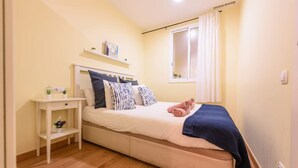 A bedroom with a bed, bedside table, and a window with curtains.