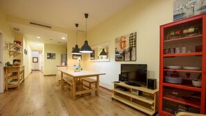 A spacious living room with a wooden dining table, a TV on a wooden stand, and a red cabinet with glass shelves.