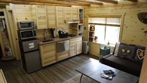 A compact kitchen with wooden cabinets, a microwave, a refrigerator, and a small dining area with a table and bench.