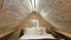 A cozy attic bedroom with a wooden sloped ceiling, a bed with white bedding and a rustic headboard, and a framed inspirational quote on the wall.