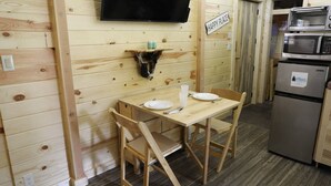 A wooden interior with a table and chairs, a mounted television, a microwave, and a refrigerator.