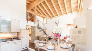 A dining area with a round table set for four, surrounded by white chairs. A staircase leads to an upper level. - Chalet Alpharmonie (Zermatt)