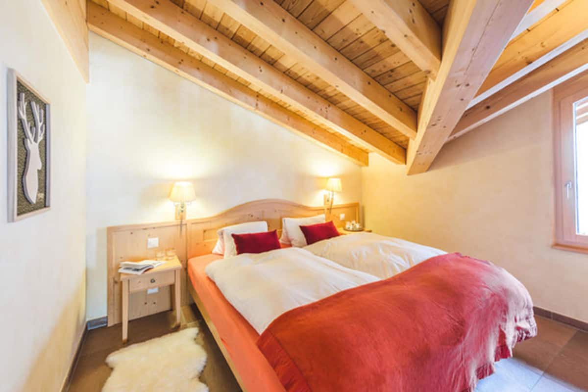 Un dormitorio con dos camas, vigas de madera en el techo, una alfombra blanca y una ventana.