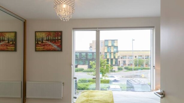A bedroom with a large window, a bed, a radiator, and two paintings on the wall.