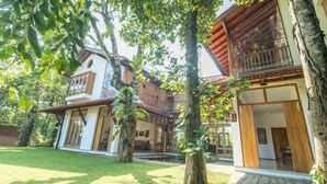Una casa de dos pisos con un balcón, rodeada de árboles y un césped cuidado.