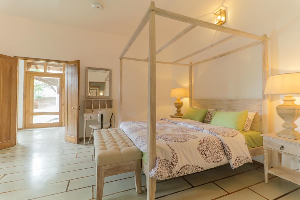 Una cama con dosel, un banco, un escritorio y una silla en una habitación con suelo de madera y un ventanal grande.