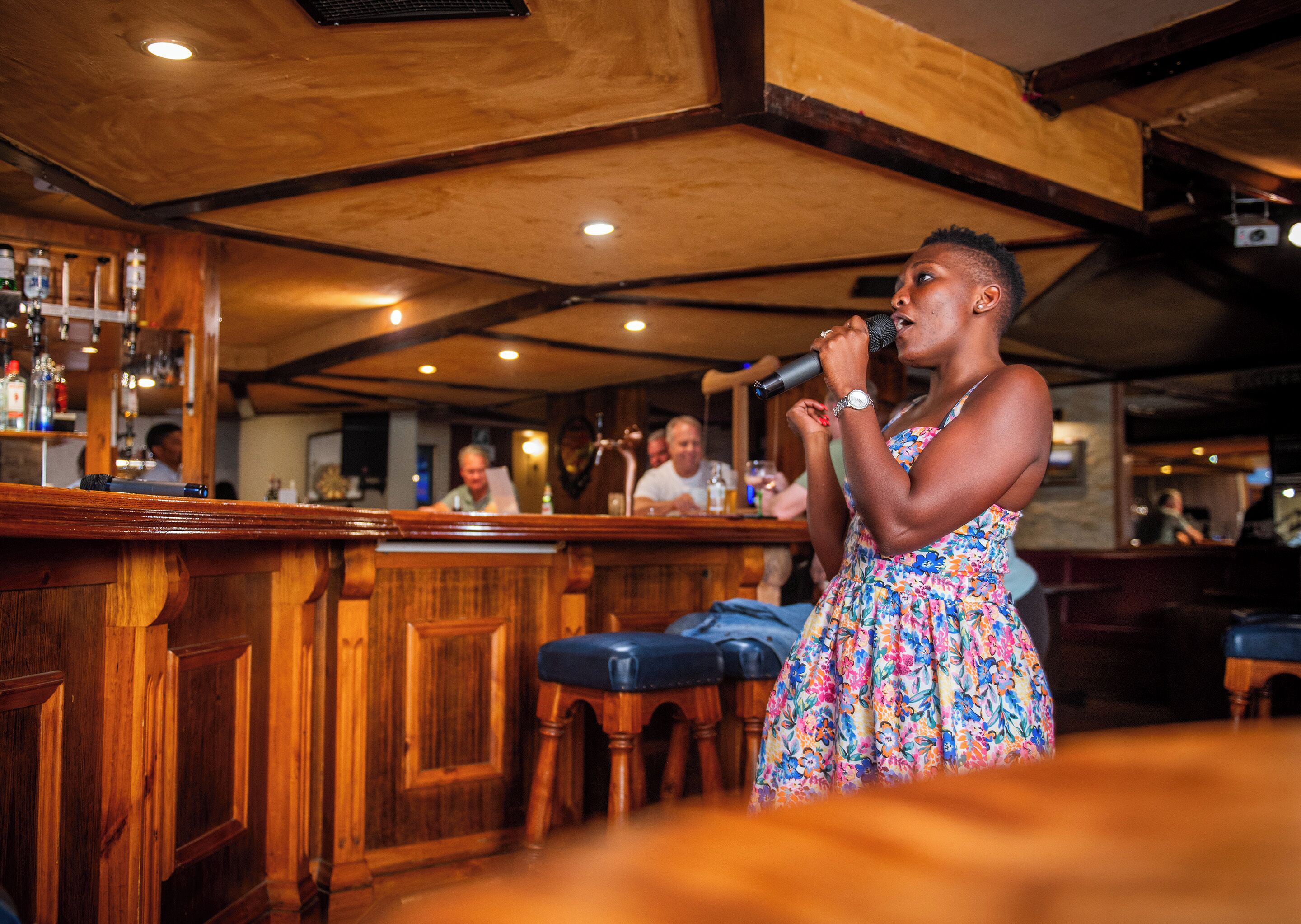 Una persona cantando en un bar con decoración de madera y taburetes.