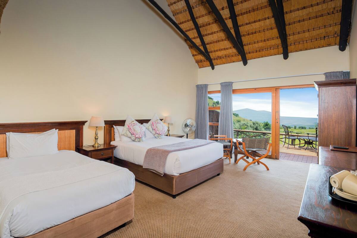 Habitación de hotel con dos camas, un balcón con vistas y techo de madera.