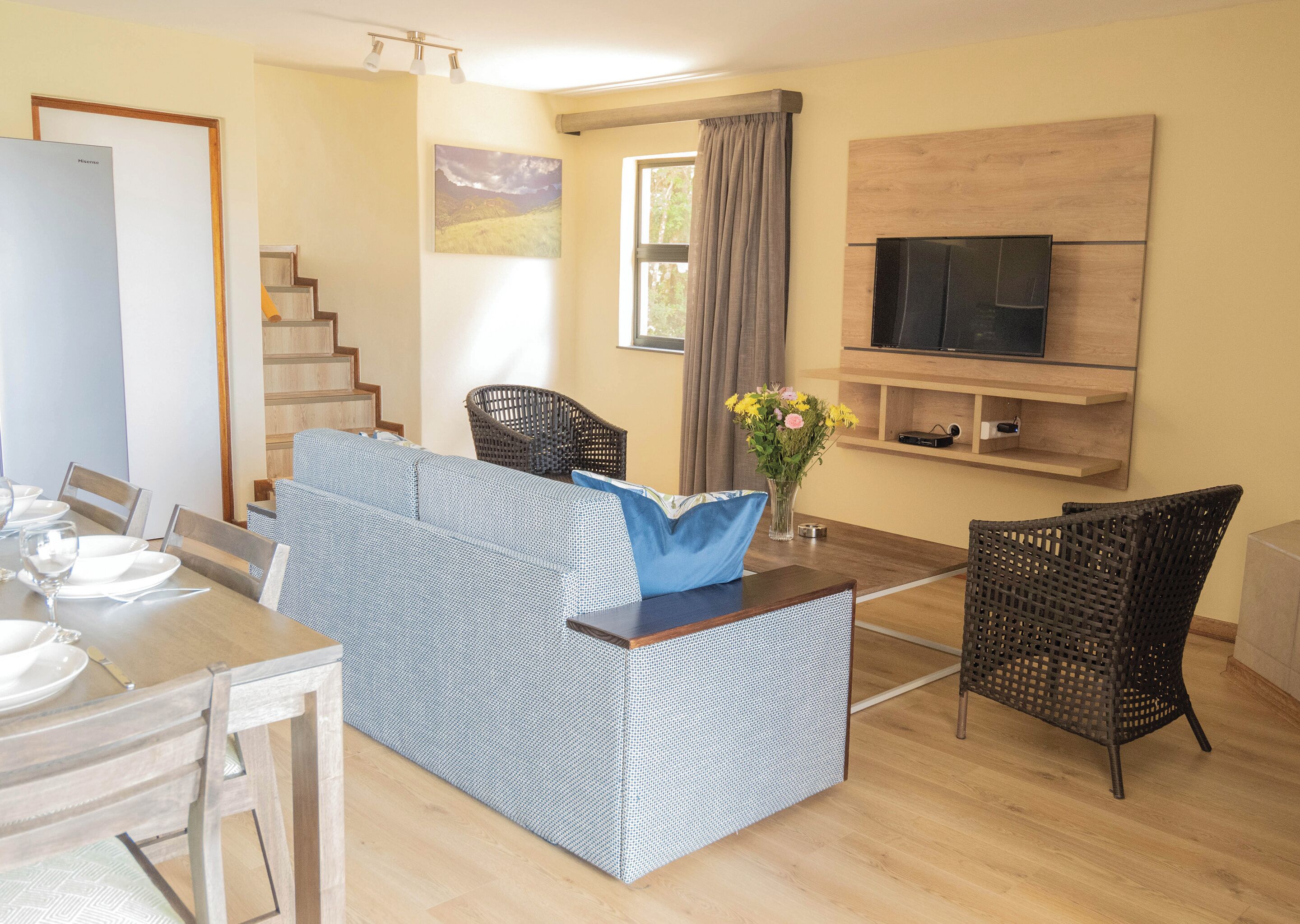 Un salon moderne comprenant un canapé, des fauteuils, une table à manger, un téléviseur et un escalier.
