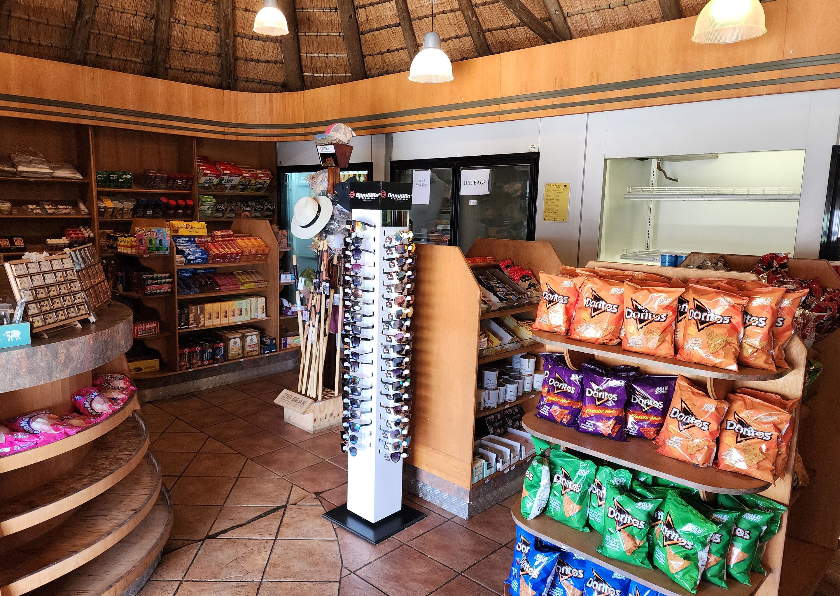 A store interior with shelves stocked with snacks, a display of sunglasses, and a sign for ice bags.