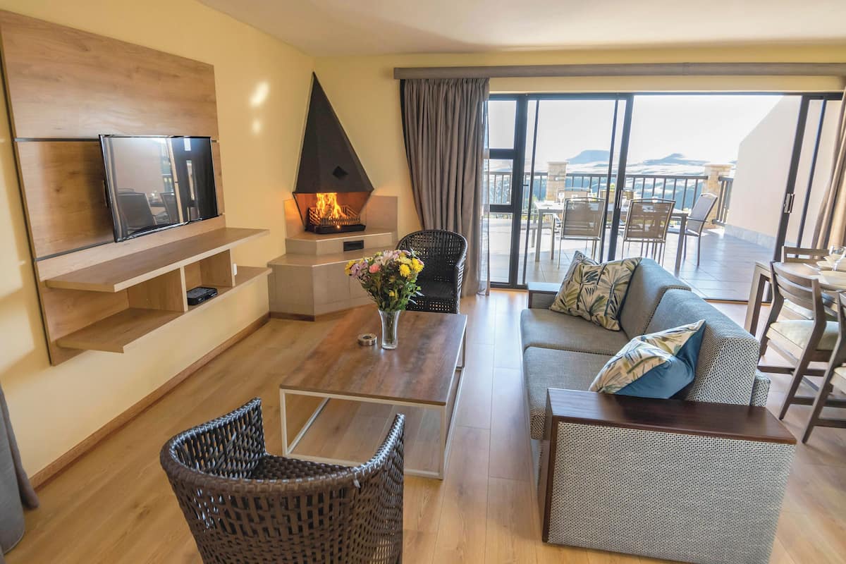 Una sala moderna con chimenea, televisor de pantalla plana, mobiliario de mimbre y un balcón con asientos exteriores.