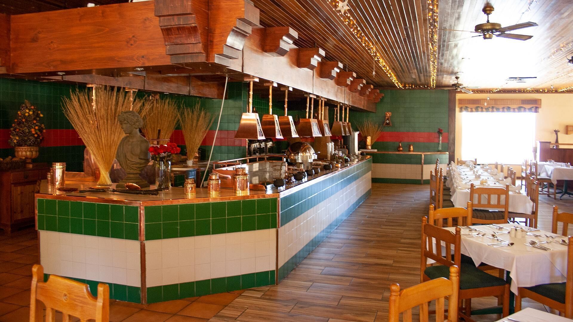 A restaurant with a central bar, wooden flooring, and a green and white tiled wall.