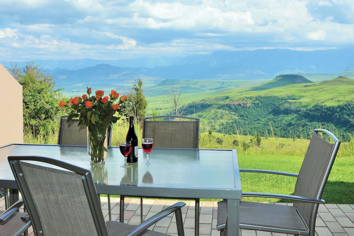 Una mesa con sillas y un jarrón de flores, con vistas panorámicas a colinas y montañas.
