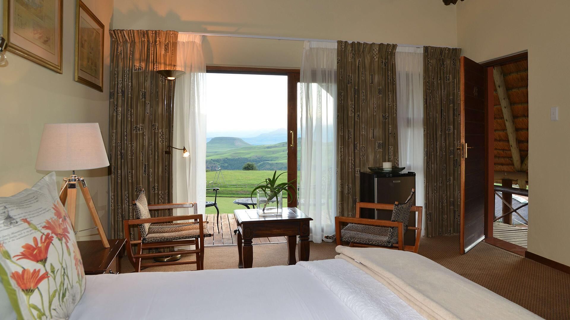 Ein Hotelzimmer mit Bett, zwei Sesseln, einem Tisch, einer Lampe und Blick ins Grüne.