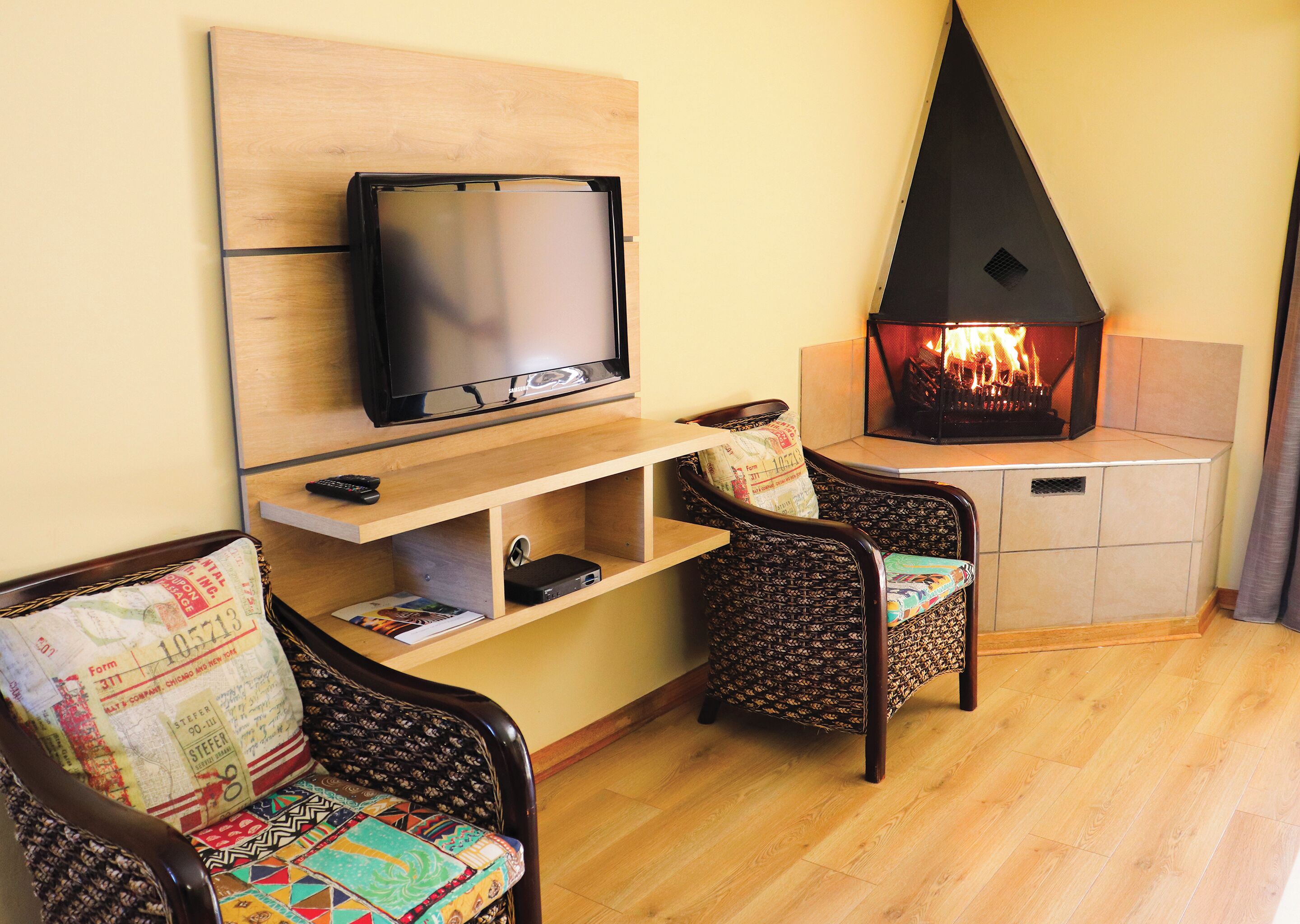 A living room with a television mounted on the wall, a fireplace, two wicker chairs, and a wooden floor.