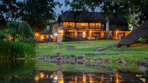 A lodge with a thatched roof, a pond in the foreground, and a well-maintained lawn. - Little Switzerland Resort (Jagersrust)