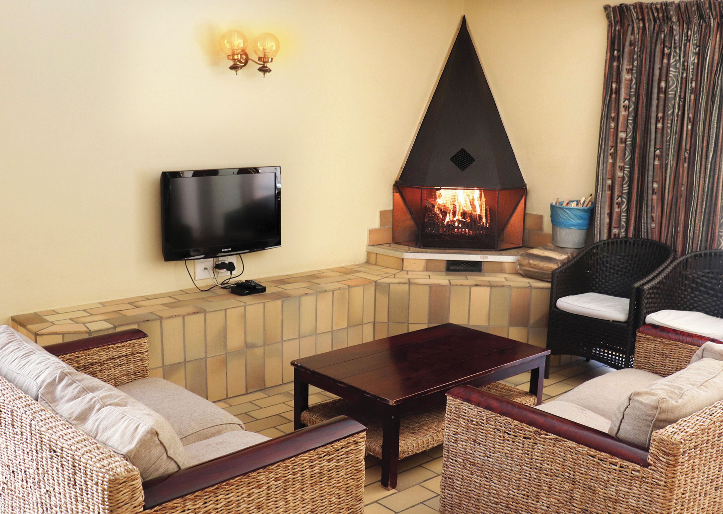A living room with a flat-screen TV, a stone fireplace, wicker furniture, and a television stand.