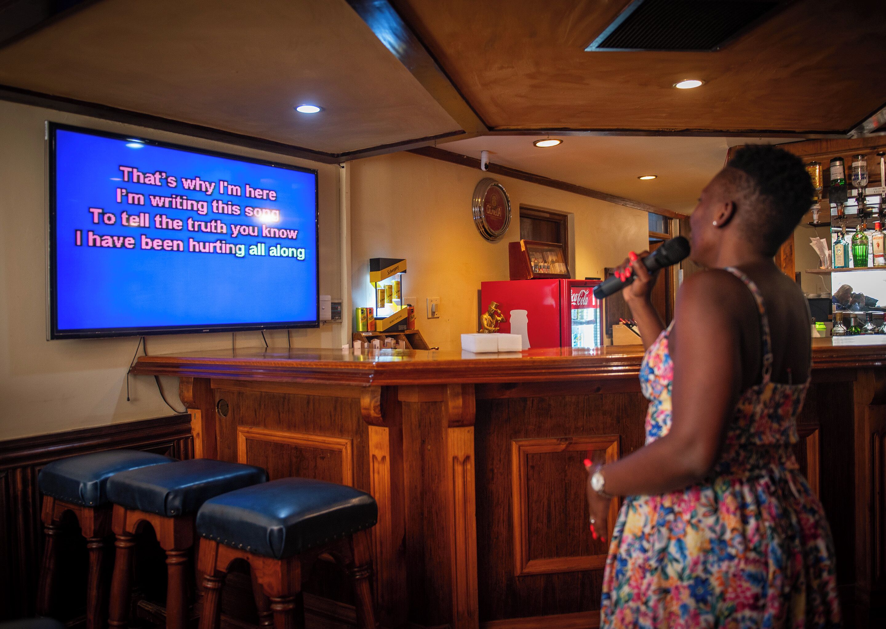 Une femme chante dans un micro dans un bar, et un grand écran affiche les paroles de la chanson.