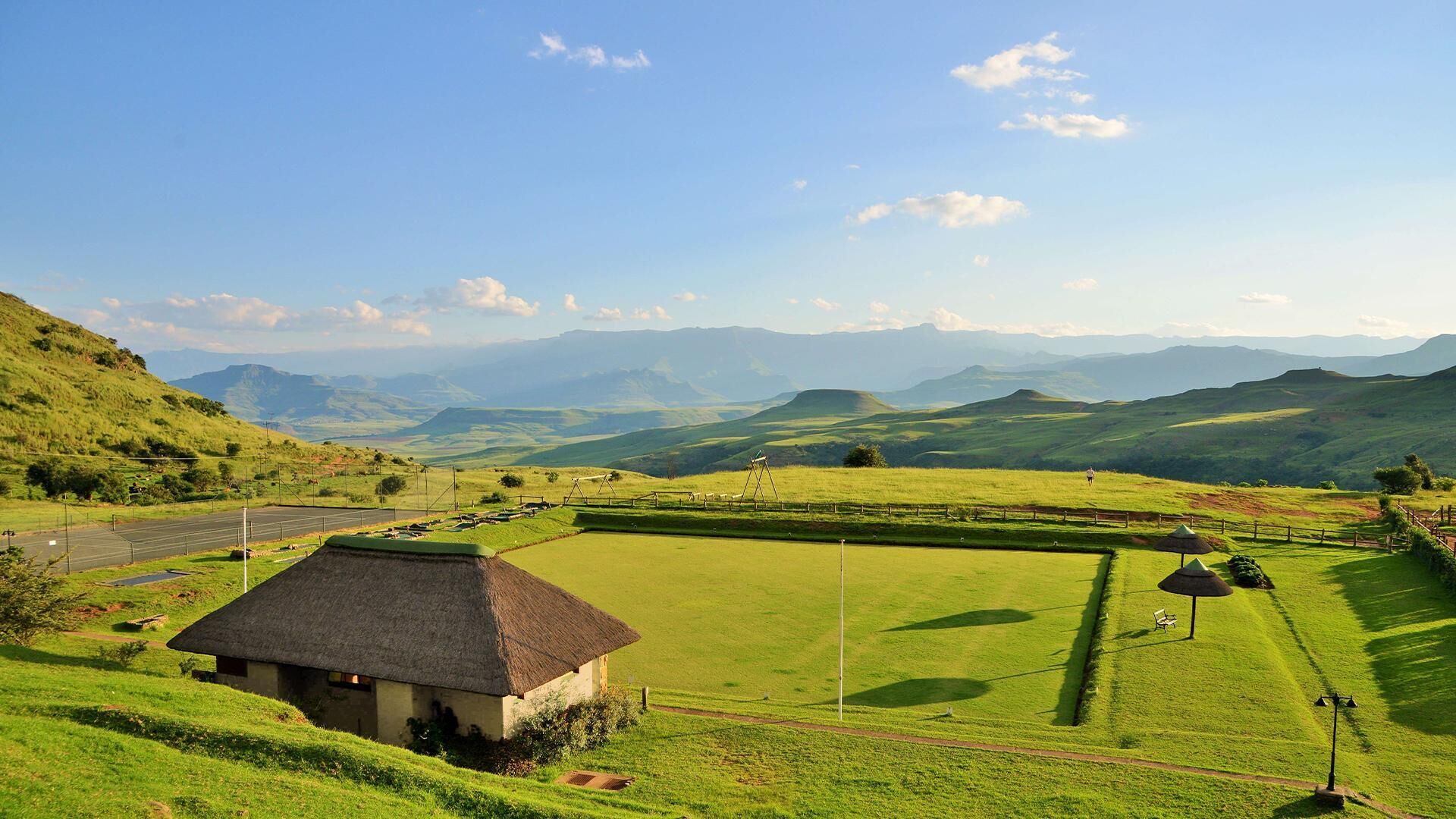 A rural landscape with a thatched-roof house, a green field, and distant mountains.