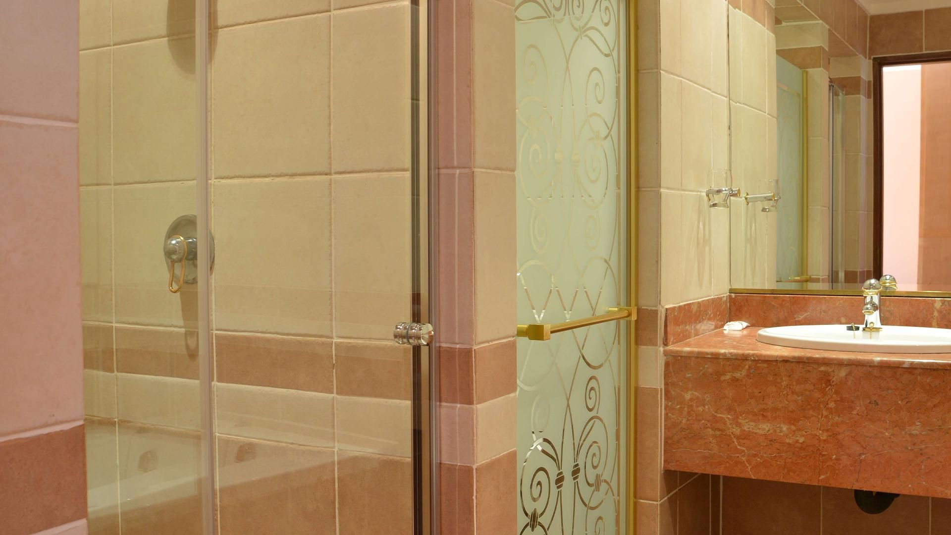 A bathroom with a glass shower enclosure, a marble sink, and a mirror.