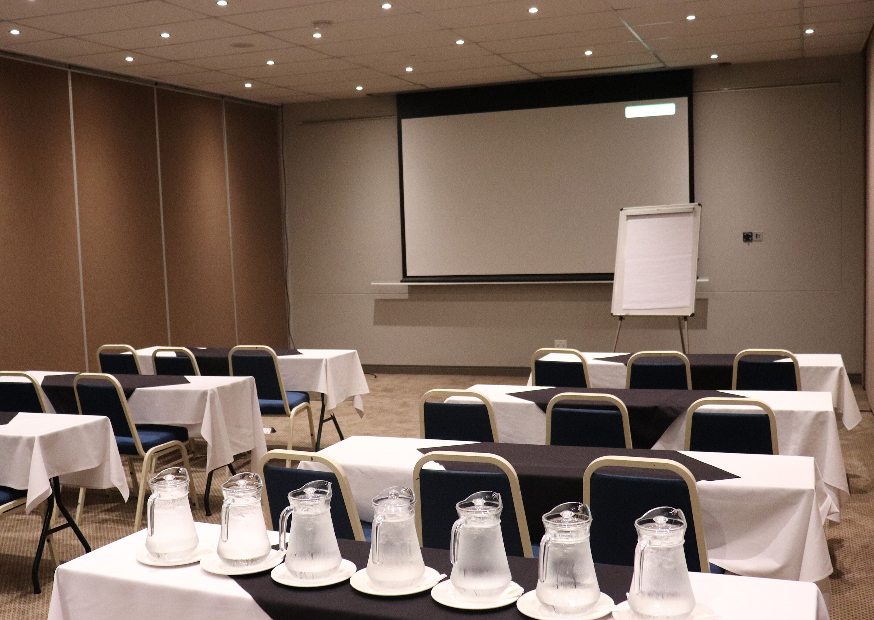 A conference room with tables, chairs, and a projector screen.