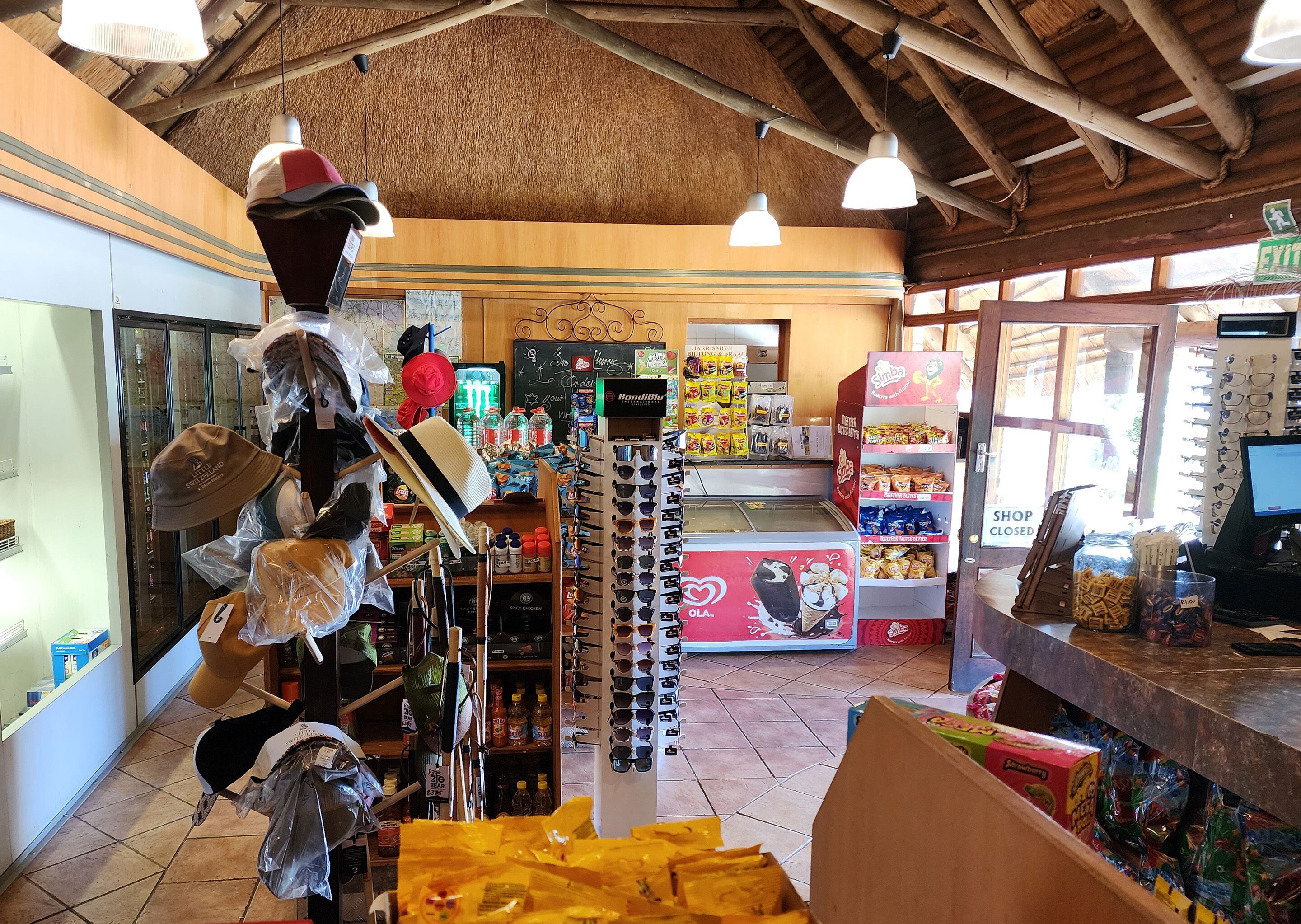 A small shop with a variety of items on display including hats, sunglasses, and snacks.
