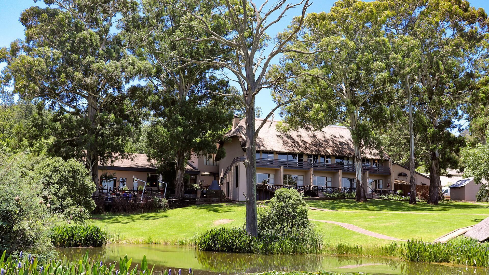 A hotel with a thatched roof, surrounded by lush greenery and a pond.