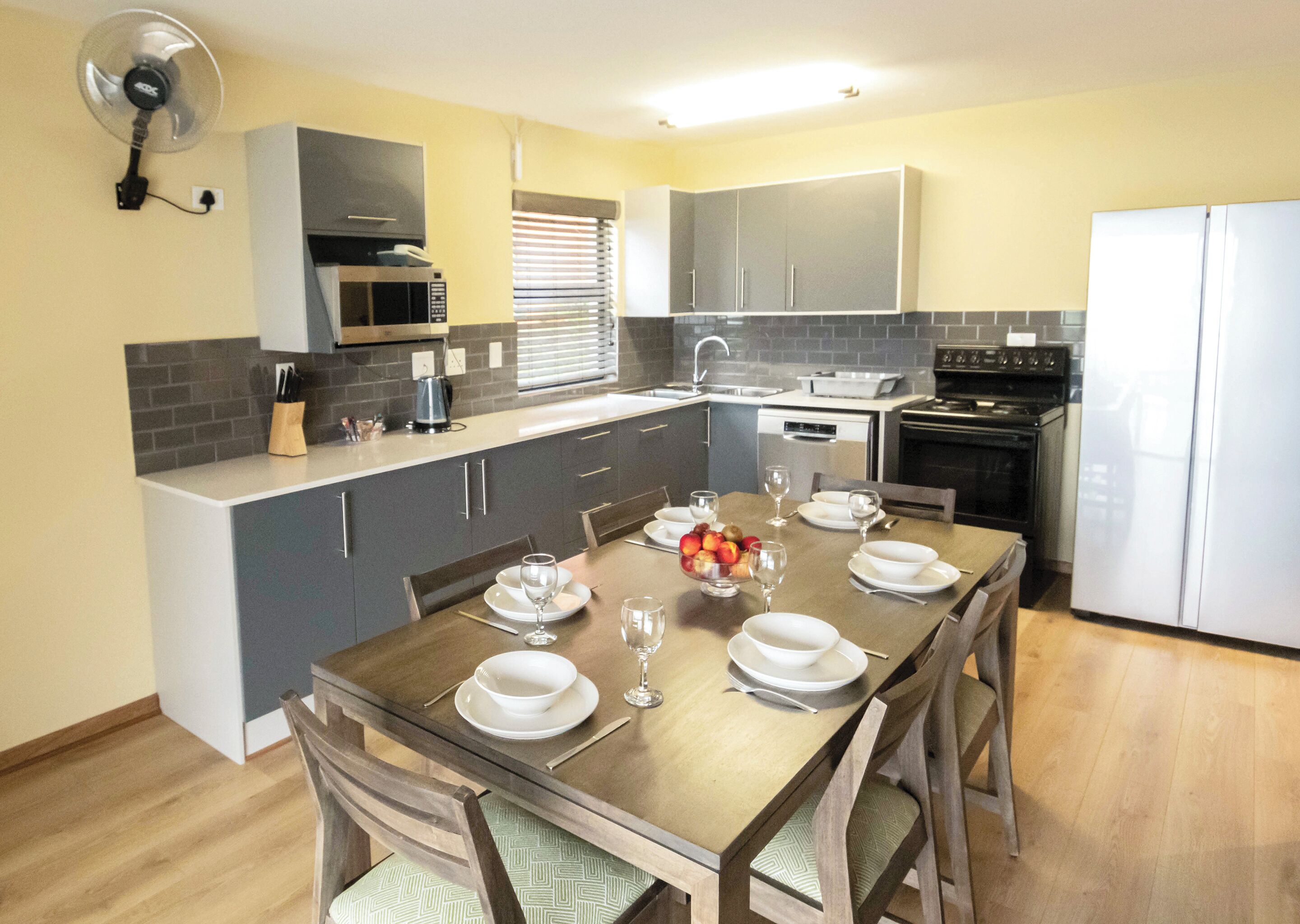 A modern kitchen with grey cabinets, a wooden dining table set for four, and a white refrigerator.