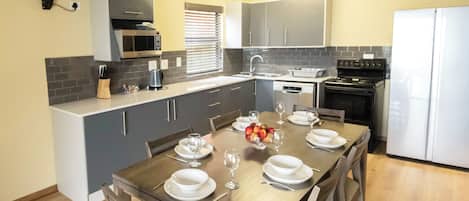 A modern kitchen with grey cabinets, a wooden dining table set for four, and a white refrigerator.