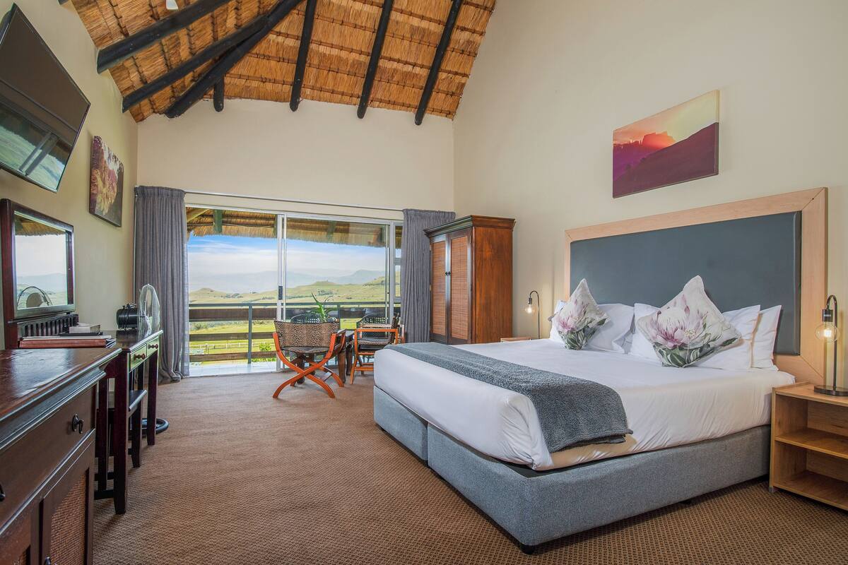 Un dormitorio espacioso con una cama grande, un escritorio y una silla, que ofrece una vista panorámica a través de un amplio ventanal.
