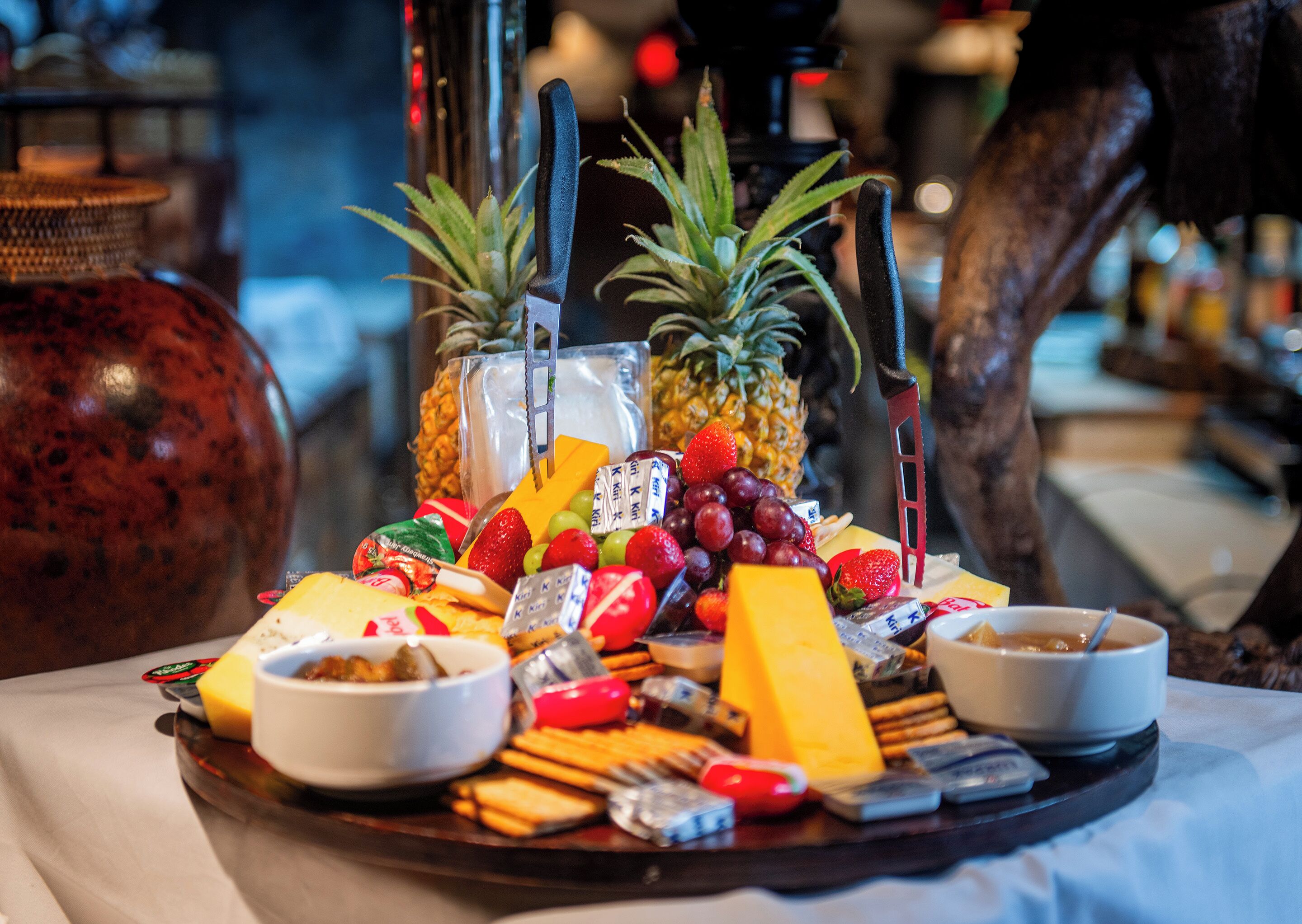 A tray of assorted snacks and fruits, including grapes, strawberries, and cheese, on a table with a white tablecloth.