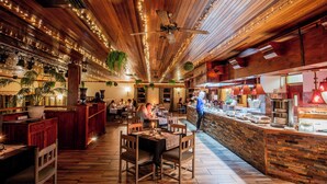 A restaurant interior with wooden floors, hanging plants, string lights, and a buffet counter. - Little Switzerland Resort (Jagersrust)