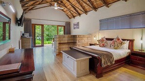 A spacious bedroom with a large bed, wooden furniture, a stone fireplace, and a view of the outdoors. - Little Switzerland Resort (Jagersrust)