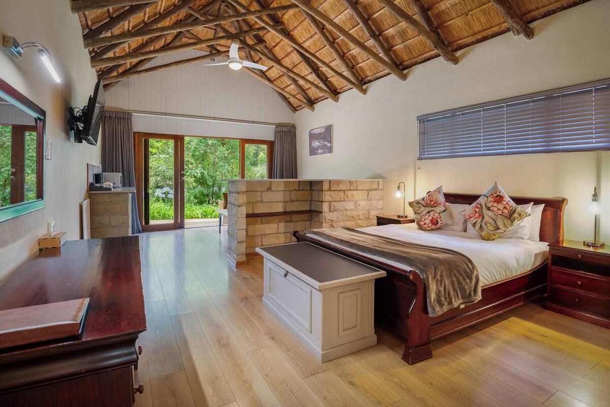 Un dormitorio espacioso con una cama grande, muebles de madera, chimenea de piedra y vistas al exterior.
