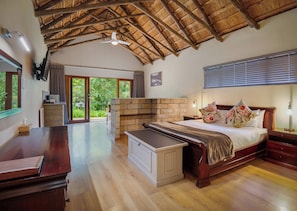 A spacious bedroom with a large bed, wooden furniture, a stone fireplace, and a view of the outdoors.