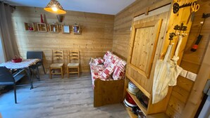 Interior acogedor de una cabaña de madera con una mesa de comedor, sillas, un banco y una zona de cocina con utensilios colgados en la pared.