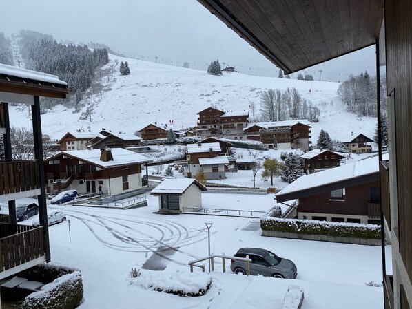 A snow-covered village with wooden buildings, a ski lift in the background, and a car parked in the foreground.