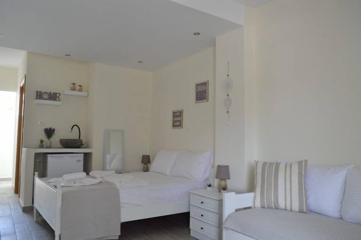 Un dormitorio con cama, mesitas de noche, escritorio y una pequeña kitchenette.