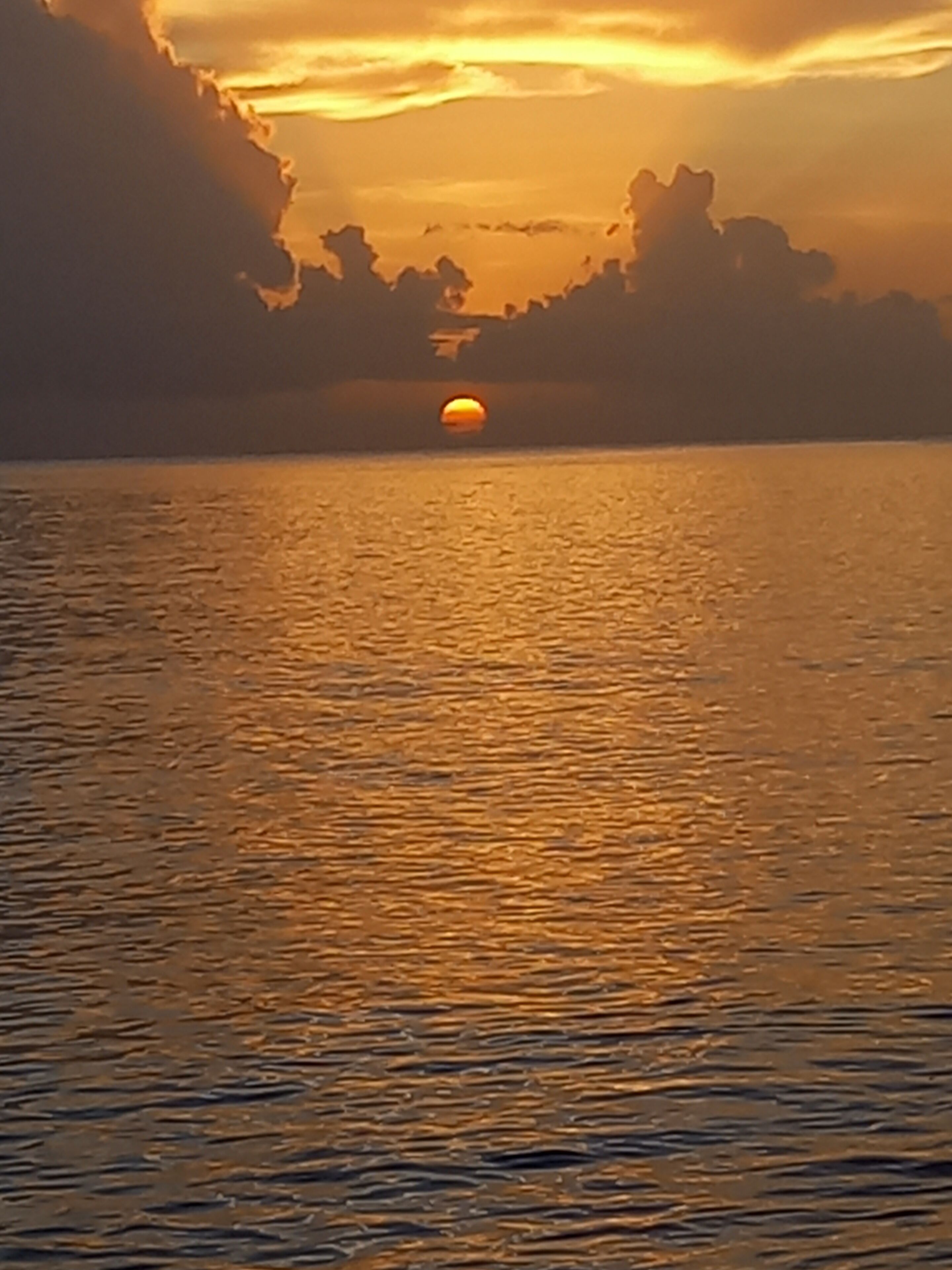 A sunset over a calm body of water with a visible sun reflection.