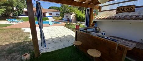 Uma área de bar ao ar livre de madeira, com uma piscina ao fundo.