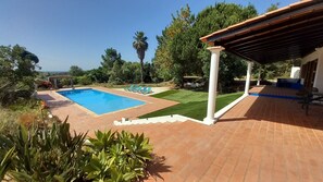 Una piscina con solárium de baldosas, un porche cubierto y vistas del paisaje circundante.