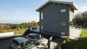A modern two-story house with a flat roof, large windows, and a garage with two cars parked inside.