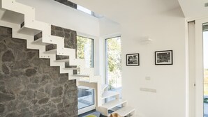 A modern interior with a stone wall, white staircase, and large windows.