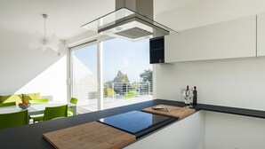 A modern kitchen with a large window, a dining area with green chairs, and a black countertop.